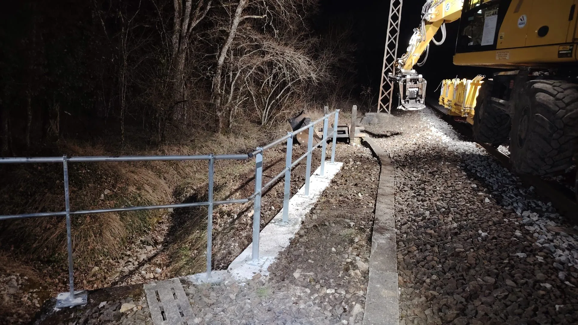 Pose de garde-corps de nuit avec pelle rail-route sur l'infrastructure ferroviaire